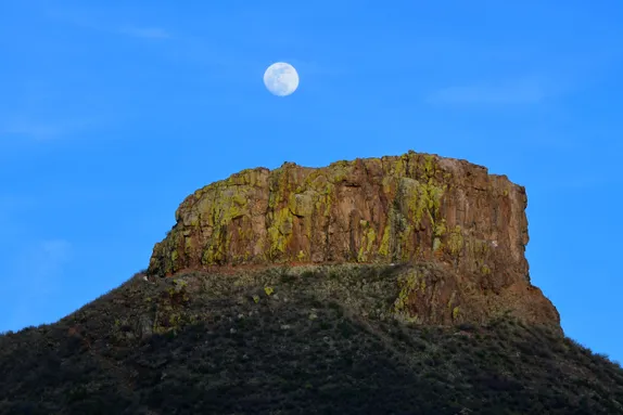 close-up of Castle Rock with a nearly-full moon overhead.  
