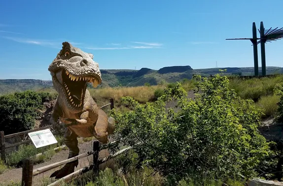 photo of Triceratops Trail, South Table Mountain in background, with clip art t-rex standing on trail