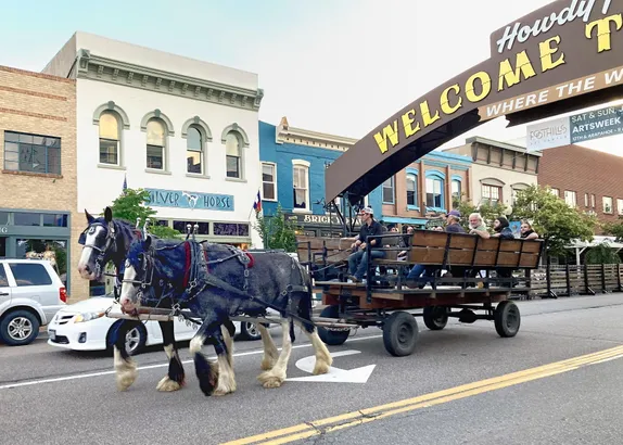 a pair of Clydesdale horses pulling a wagon through downtown Golden