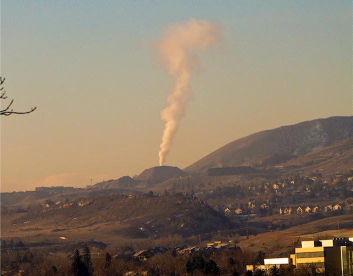 A cone-shaped mountain near Golden, Colorado with a plume of white smoke rising straight up.