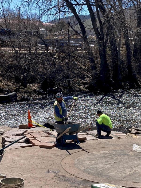 Two city workers repairing stonework along Clear Creek on a sunny spring day