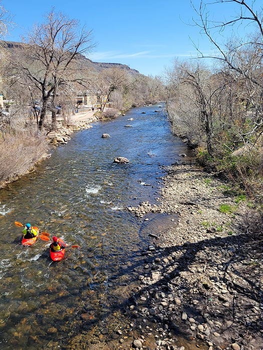 Looking east on Clear Creek in Golden Colorado.  Two kayakers are padding in very clear, shallow water.