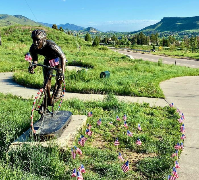 Bronze statue of a bicyclist and American flag decorations - South able Mountain in the background