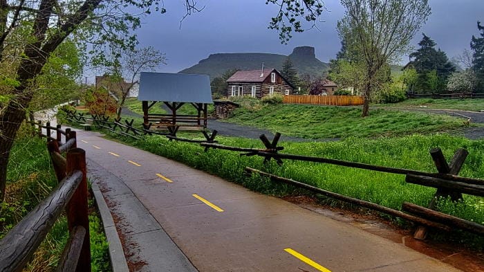 Clear Creek History Park with very green grass, South Table Mountain in the background and bike/pedestrian trail in the foreground, overcast sky