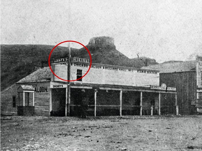 Cheney's Chicago Saloon with signs offering billiard games.  Castle Rock in the background.