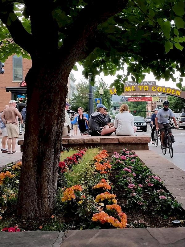 Planter box filled with flowers at 1200 Washington Avenue.  People on bikes, and the Welcome Arch in the background