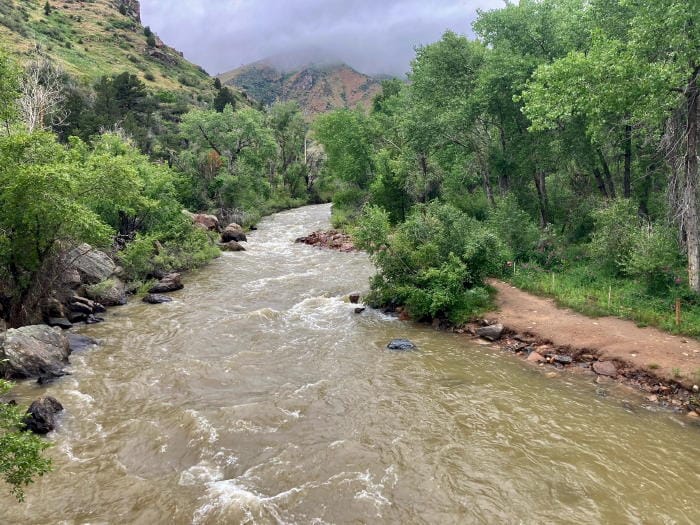 Clear creek, muddy with turbulence from recent rains.  Mountains in the background are partially obscured by low-hanging crowds.