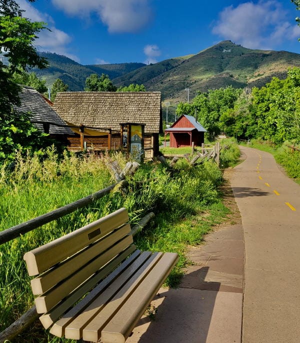 Clear Creek Trail & History Park with Mt. Zion in the background, a bench in the foreground, and a bright blue summer sky.