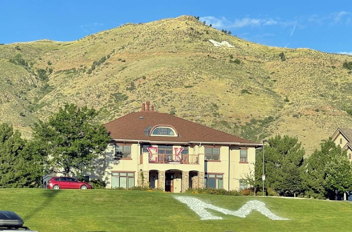 A stone M is embedded in the lawn in front of the Sigma-Kappa house on the School of Mines campus.  In the background, the larger M emblazons Mt. Zion.