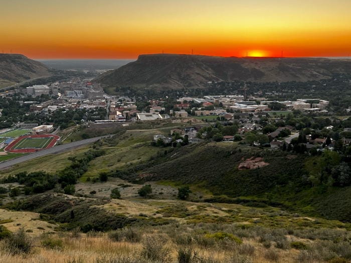 The sun peeping over South Table Mountain.  The sky is orange and the Golden valley is still in shadow.