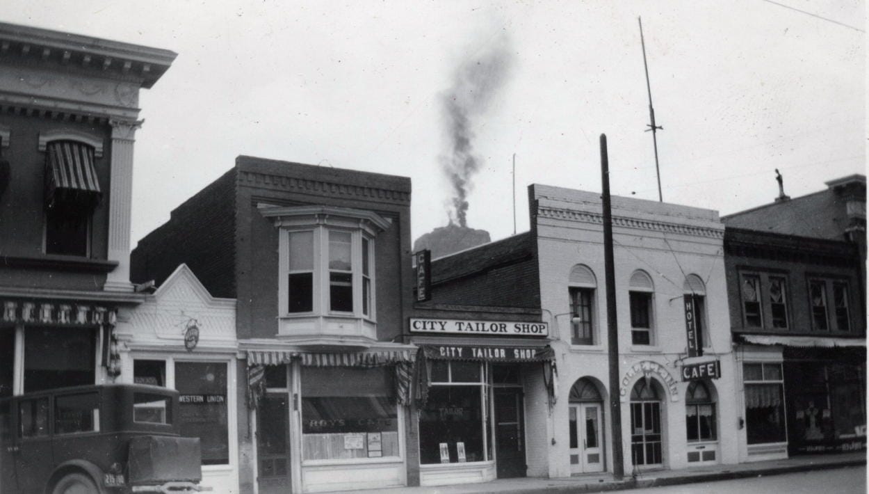 brick storefronts - above and behind is Castle Rock with a plume of smoke rising