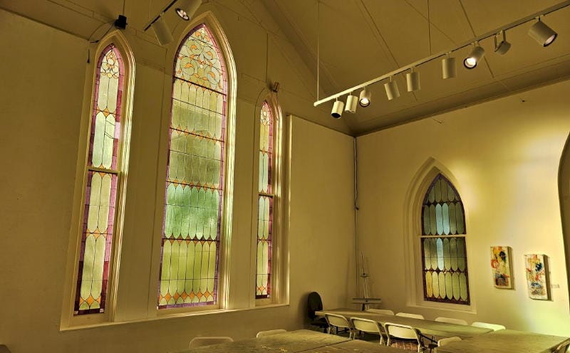 room with folding chambers and chairs and tall, multi-paned gothic style stained glass windows