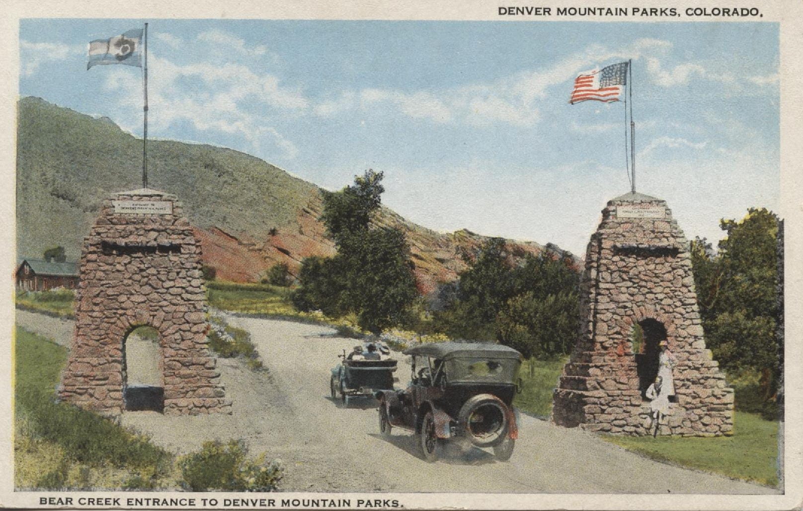 hand-tinted postcard showing two stone pillars with American and Colorado flags, two 1920s cars, and two girls