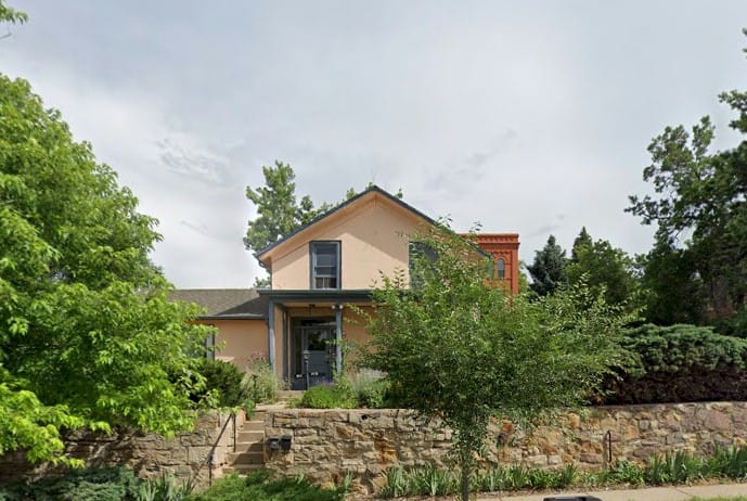 peach colored Victorian frame house with front porch and stone retaining wall in front