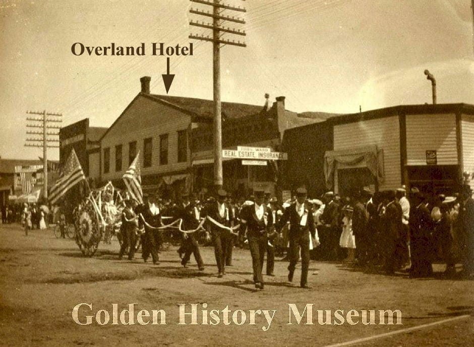 A team of men in uniforms pulling a hose cart.  The cart is decorated in bunting & American flags.