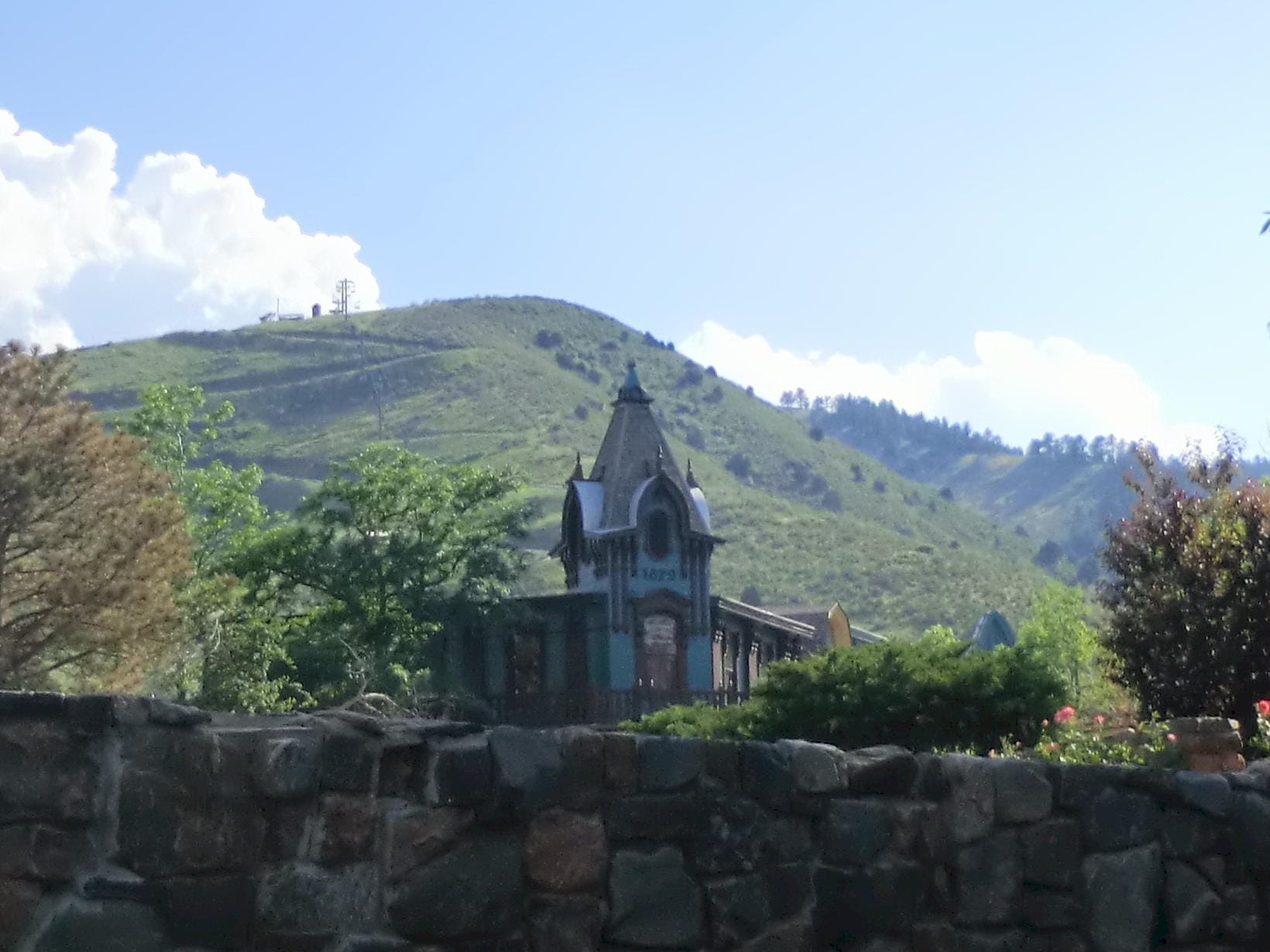 stone wall in the foreground, Victorian building with turret, mountain with alpine slide in background