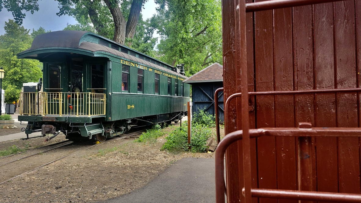 wooden freight car on the right side and green passenger car with rear balconcy on the left