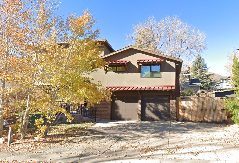 Two story tan house with garage under one section and a tall wooden gate providing access to a side yard