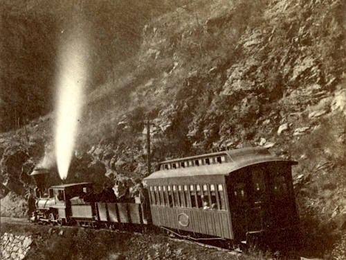 steam locomotive in canyon with one freight and one passenger car