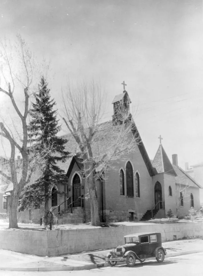 Antique photo of a small brick church with a 1920s-era car parked at the curb