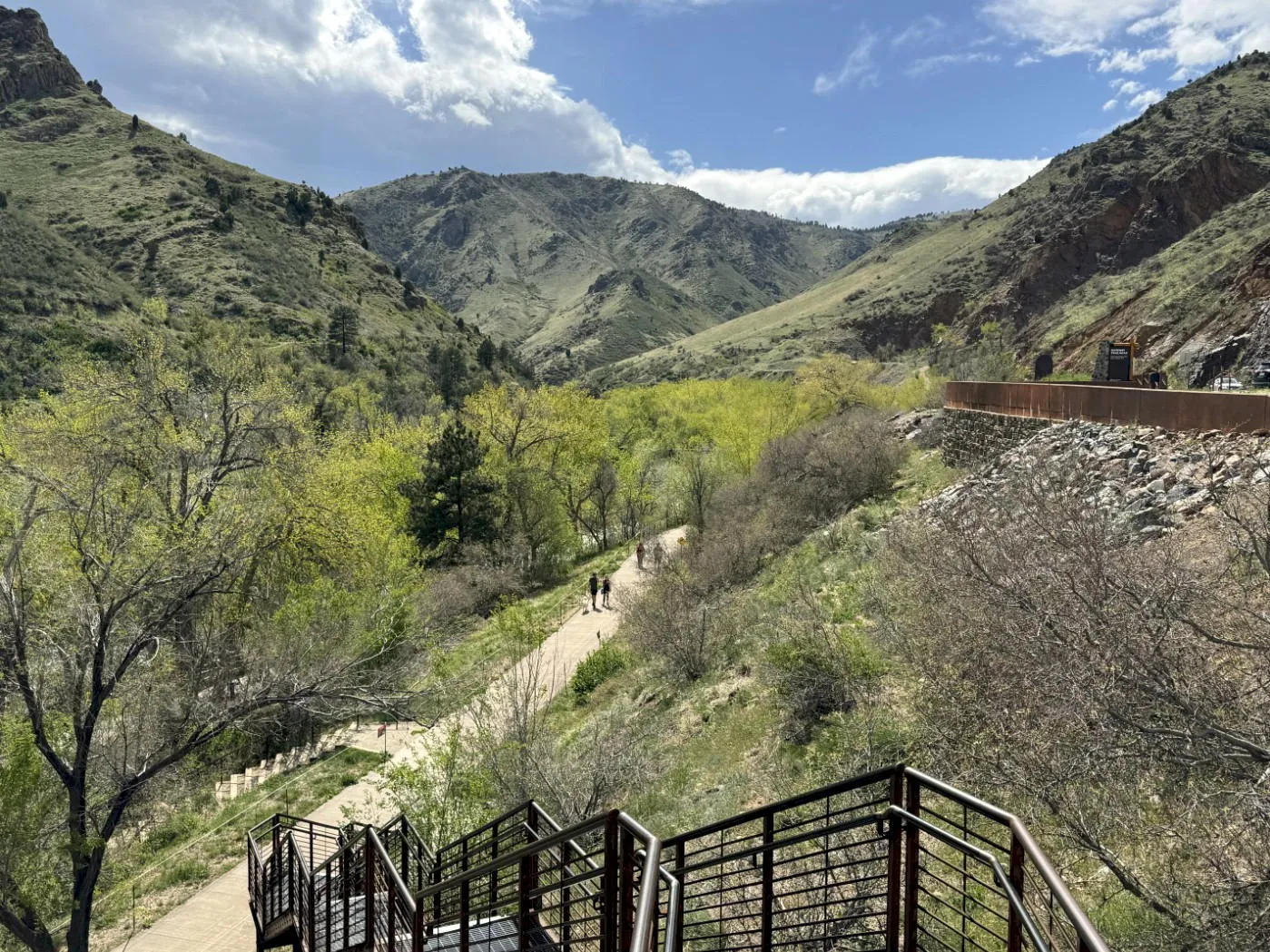 view down into a canyon with a concrete trail from the top of a long set of metal stairs. Viewer is above the treetops.