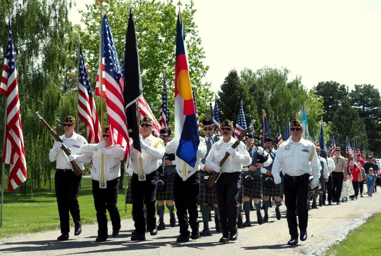 parade of people led by color guard with flags, followed by a pipe and drum corps
