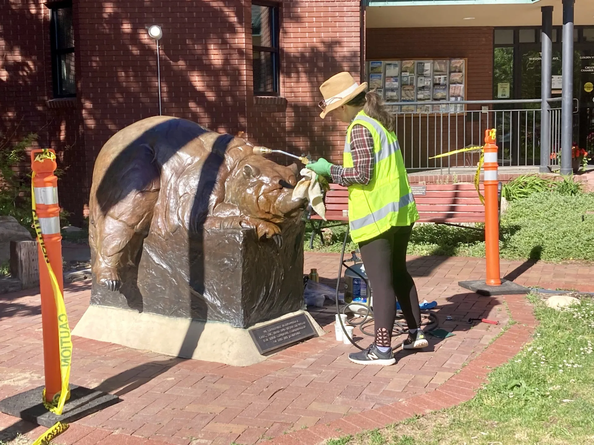 woman in a yellow vest polishing a bronze statue of a bear in front of the Visitors Cent