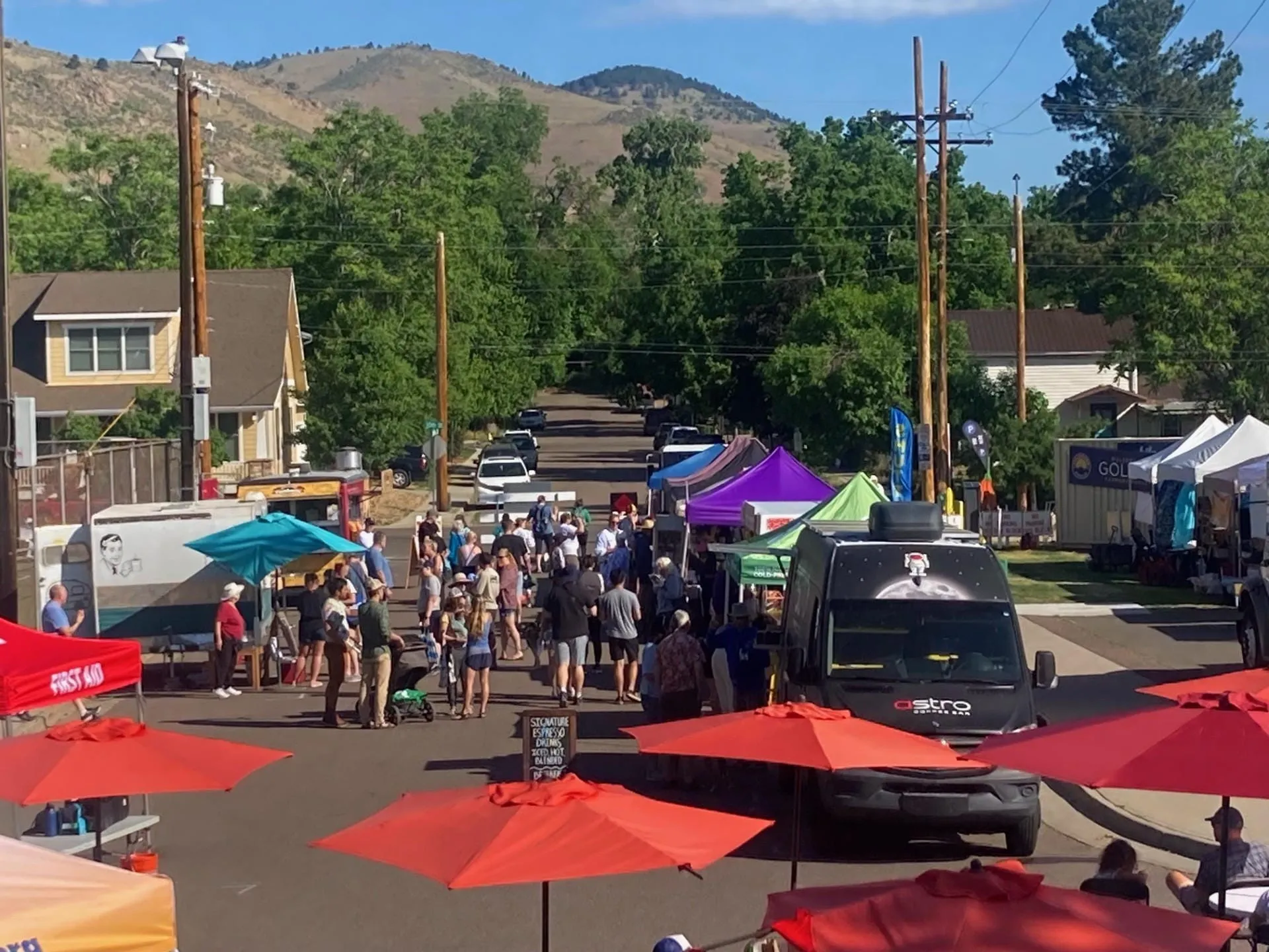 booths, colorful umbrellas, a small crowd of shoppers, and the mountains in the background