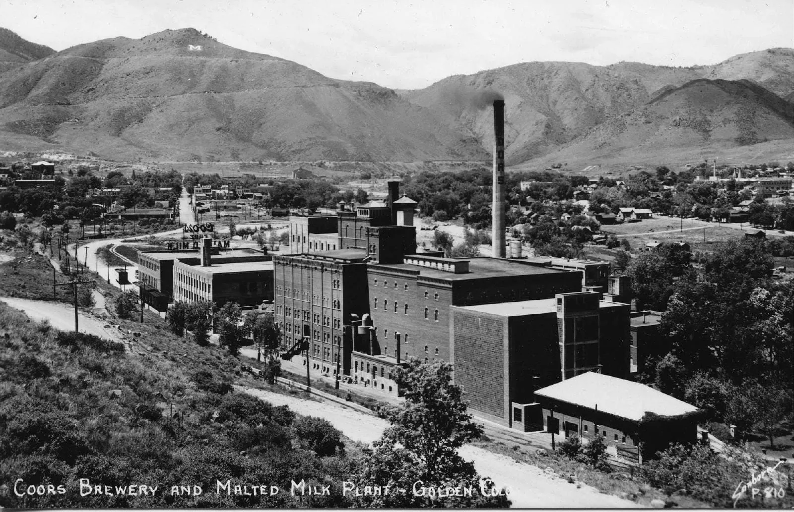 Coors brick brewery, 1930s, with a smokestack producing smoke and Mt. Zion with the M in the background