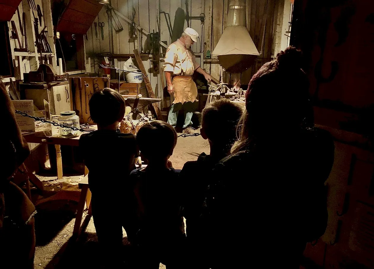 silouettes of children standing in the doorway with a blacksmith at his forge in the background