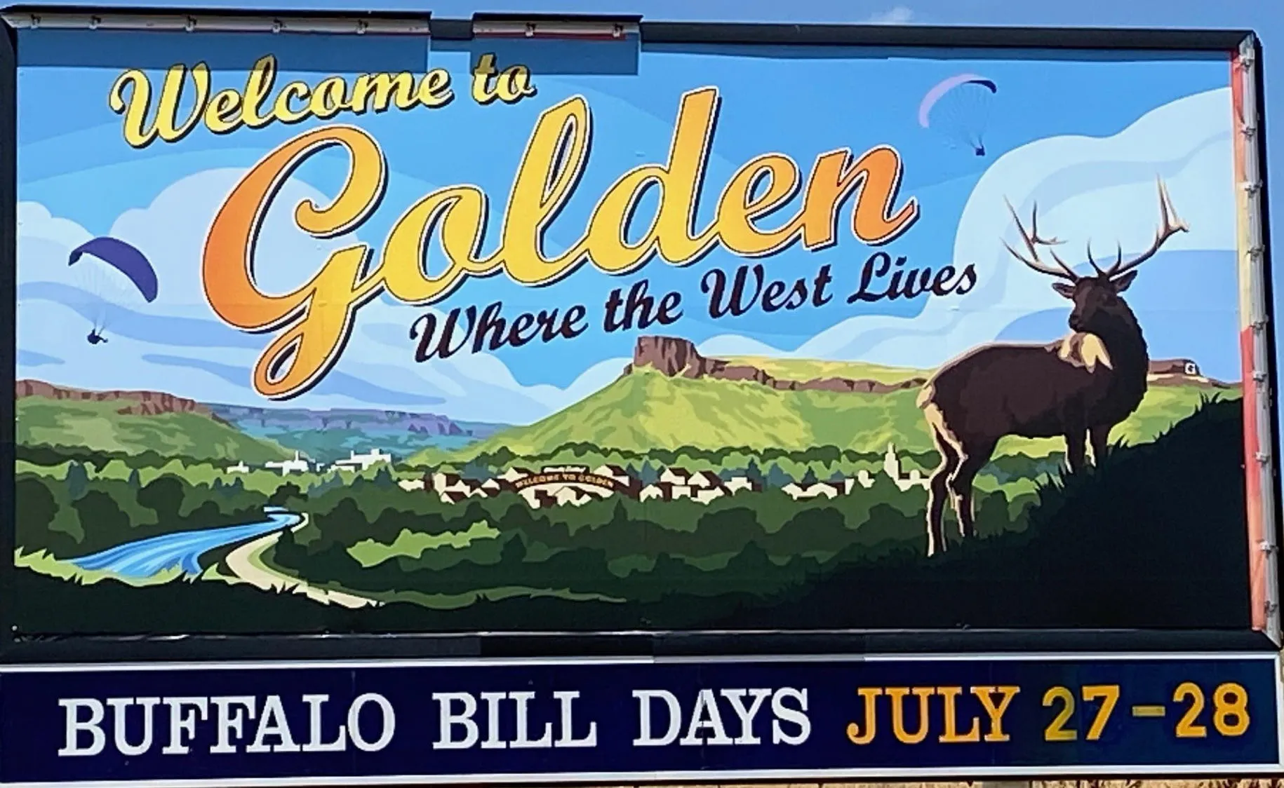 billboard with a cartoon image of Golden, including the mountains, hang gliders, Clear Creek, arch, and a stag