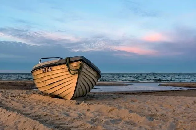 wooden boat on a beach by the ocean - sunset sky