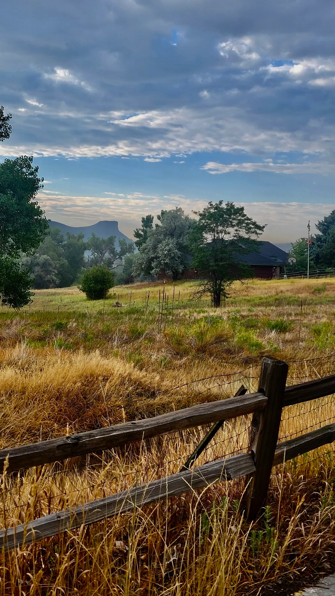 split rail fence and dry grass in the foreground, green meadow and trees mid-distance, and Castle Rock in background