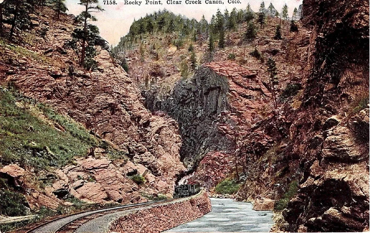 colorized image showing a narrow gauge track and locomotive running through a canyon, parallel to a mountain strem