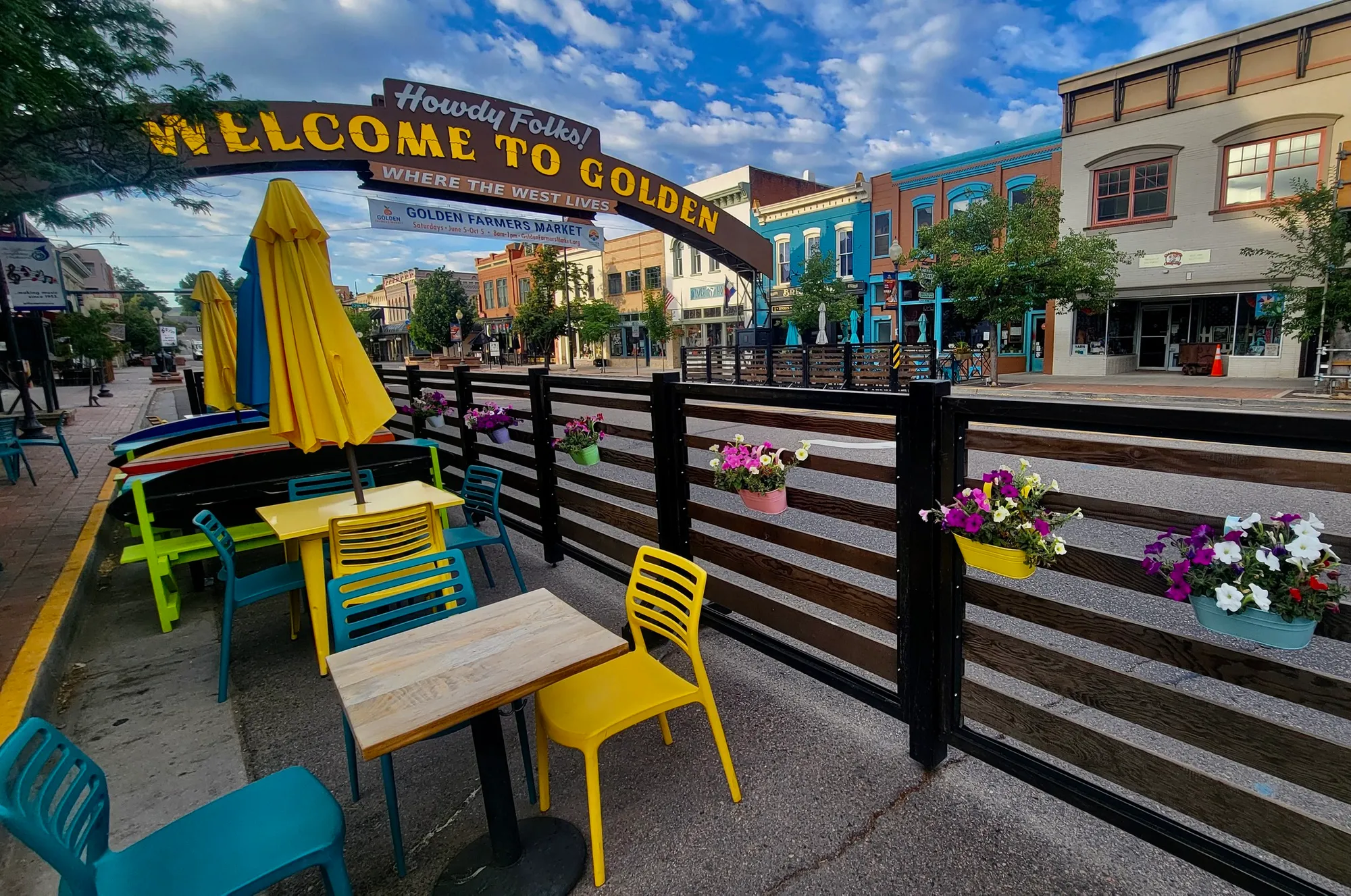 view of the Golden Welcome arch with tables and flowers in foreground, 19th-century buildings in background