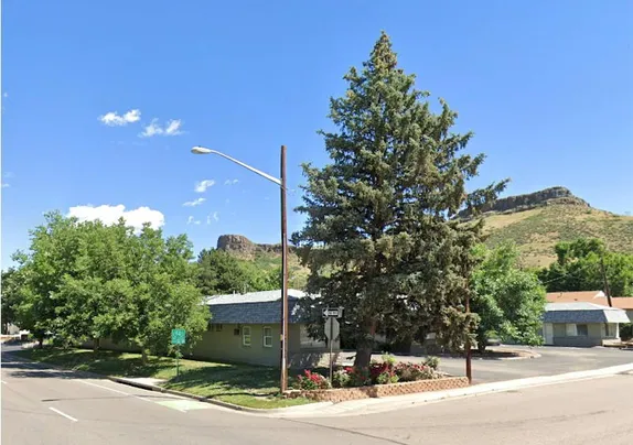 U-shaped one story building with large trees along Ford Street, rose bushes, and South Table Mountain in the background