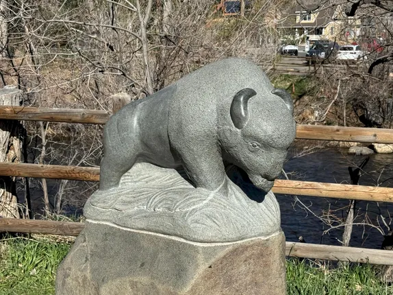 stone statue of a buffalo with split rail fence and Clear Creek in the background