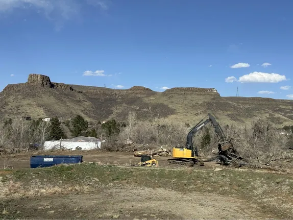 heavy equipment moving felled trees - dumpster nearby - South Table Mountain in the background