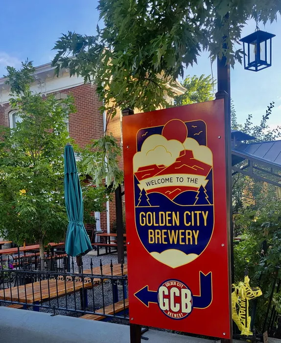Red and Blue Golden City Brewery sign with 2-story red brick house and picnic tables in background
