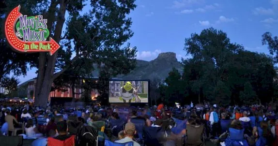 evening - crowd of people in lawn chairs facing a movie screen showing Shrek - Castle Rock in the background