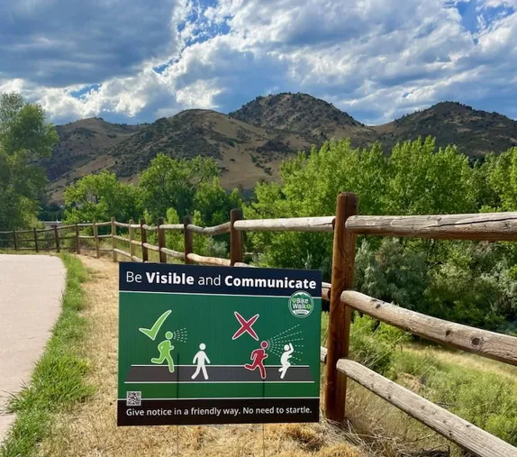 trailside sign saying "Be Visible and Communicate - Give notice in a friendly way. No need to startle."