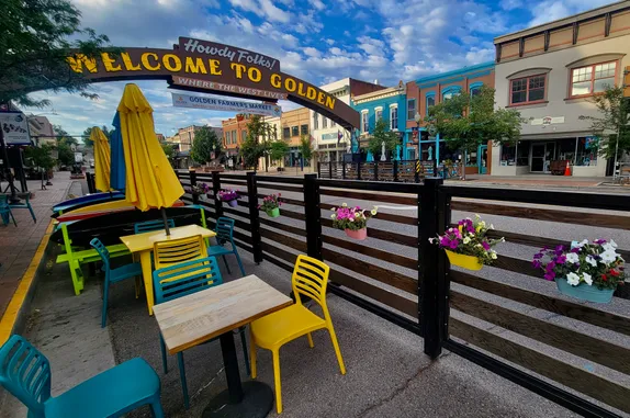 view of the Golden Welcome arch with tables and flowers in foreground, 19th-century buildings in background