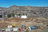 construction site, mostly dirt, with pile of dead trees, construction equipment, dumpters, Castle Rock in the background